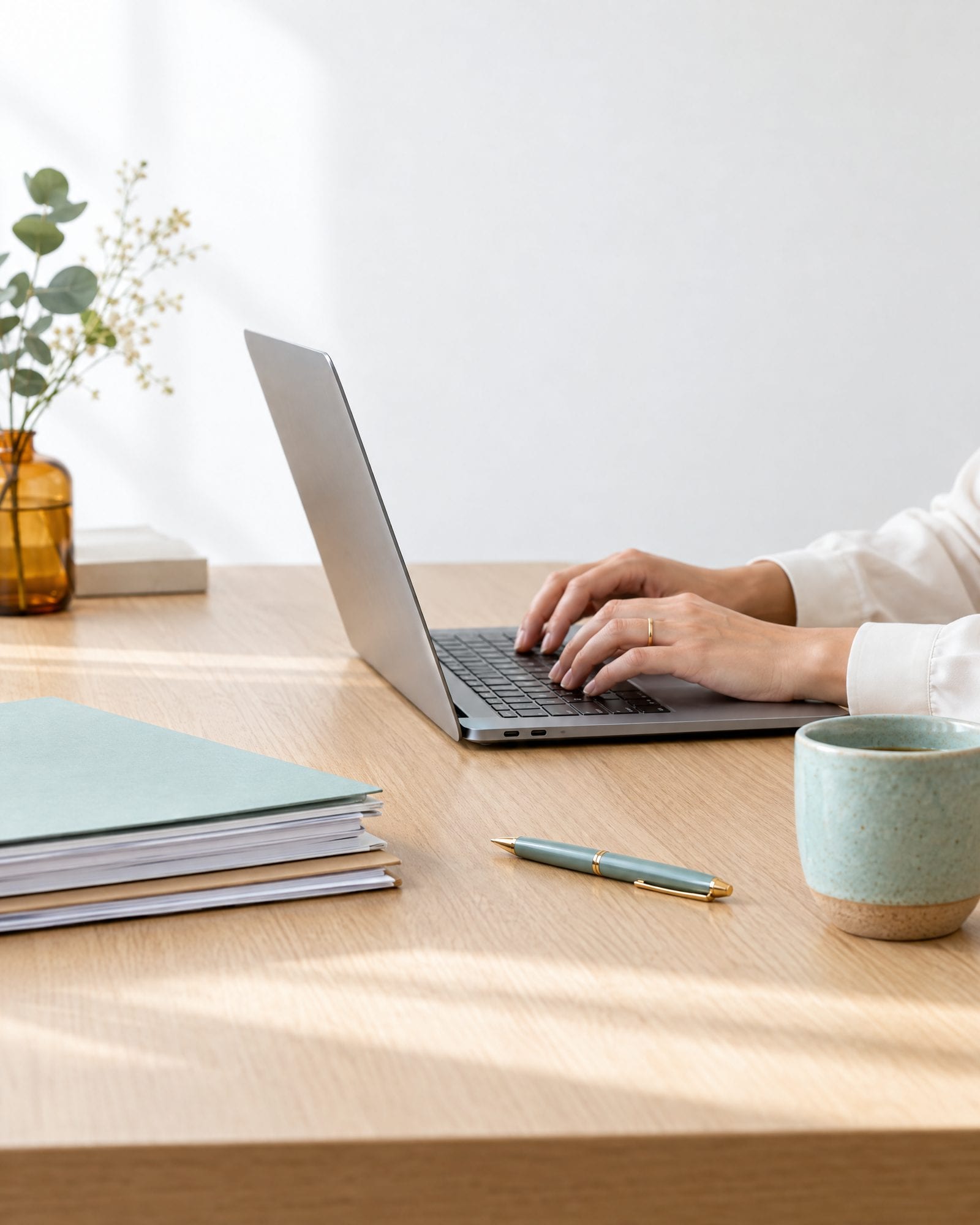 Hands typing on a laptop beside a neat folder of documents